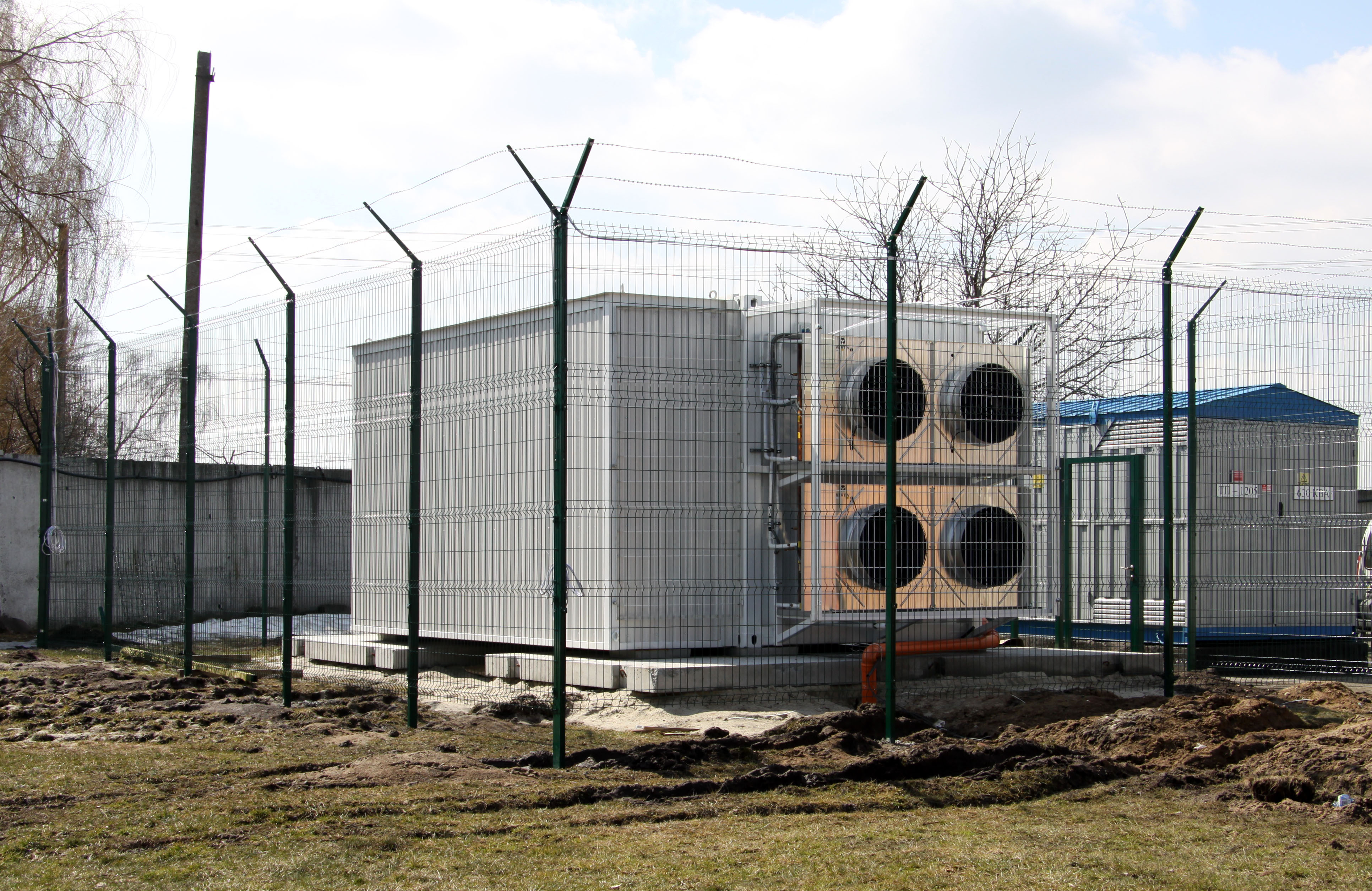 Exterior of compact modular data center with cooling fans behind security perimeter fencing in field environment