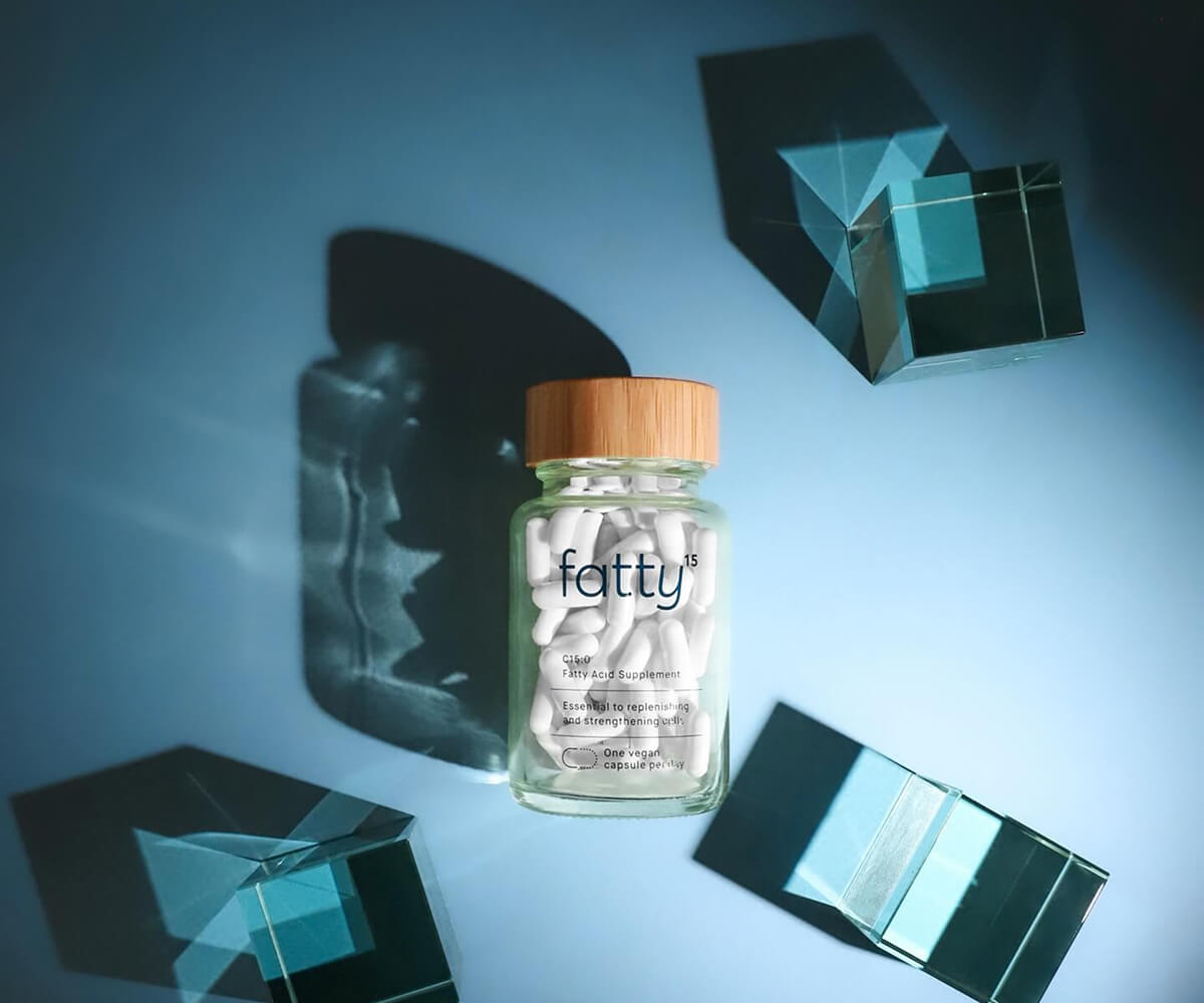 Glass bottle of fatty acid supplement capsules with a wooden lid on a blue surface surrounded by translucent blue cubes casting shadows.