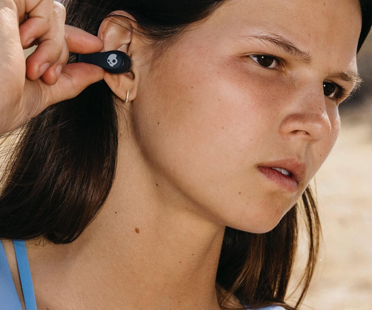 Close-up of a woman inserting a black Skullcandy wireless earbud into her ear.