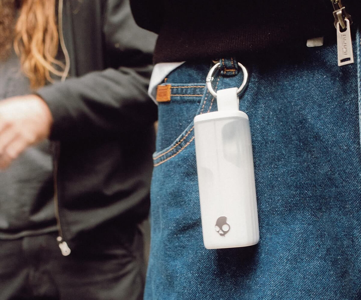 White Skullcandy portable speaker attached to the belt loop of blue jeans.