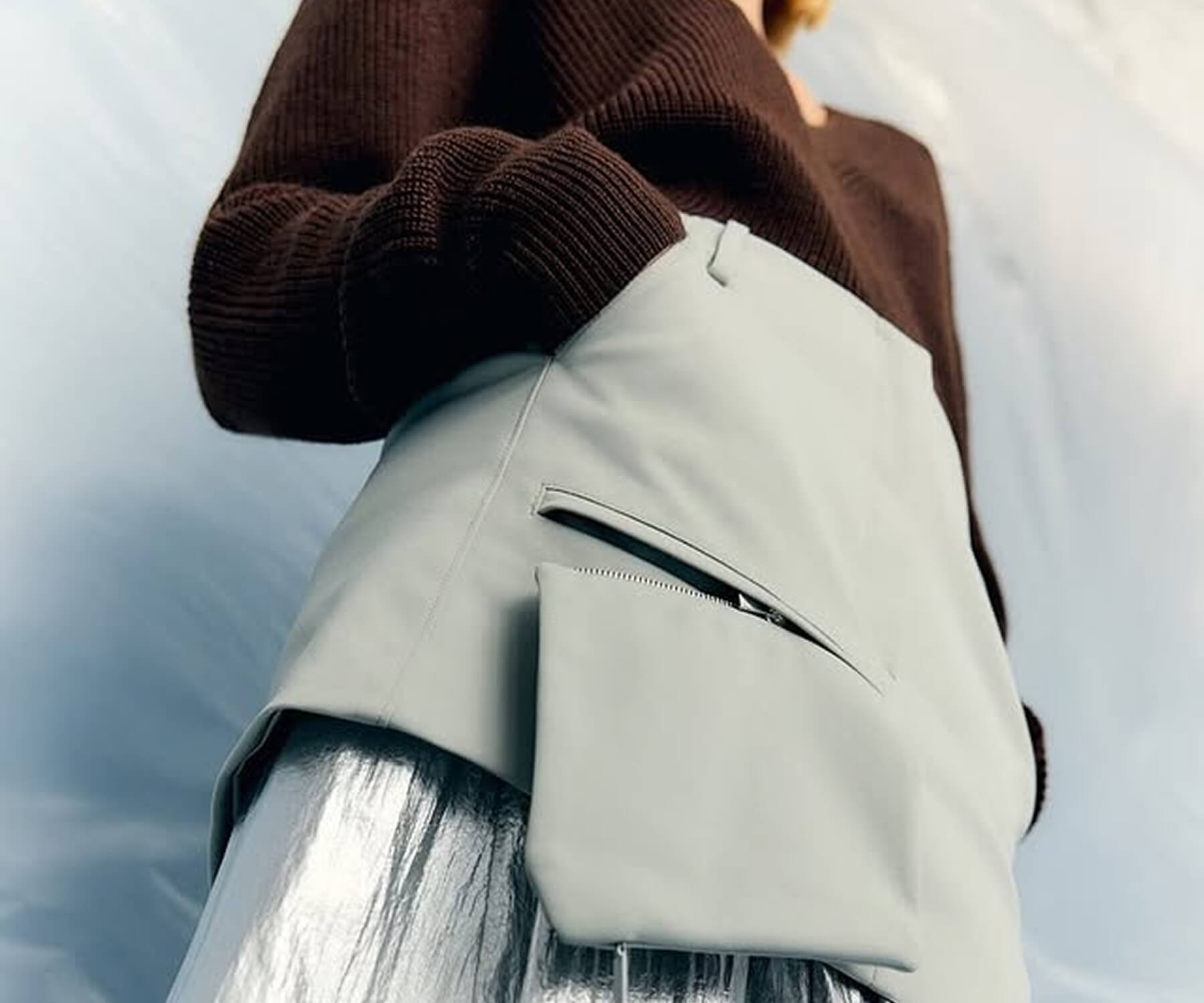 Young man and woman dressed in black and gray carrying matching gray bags with a textured pattern, standing in front of a circular-patterned wall.