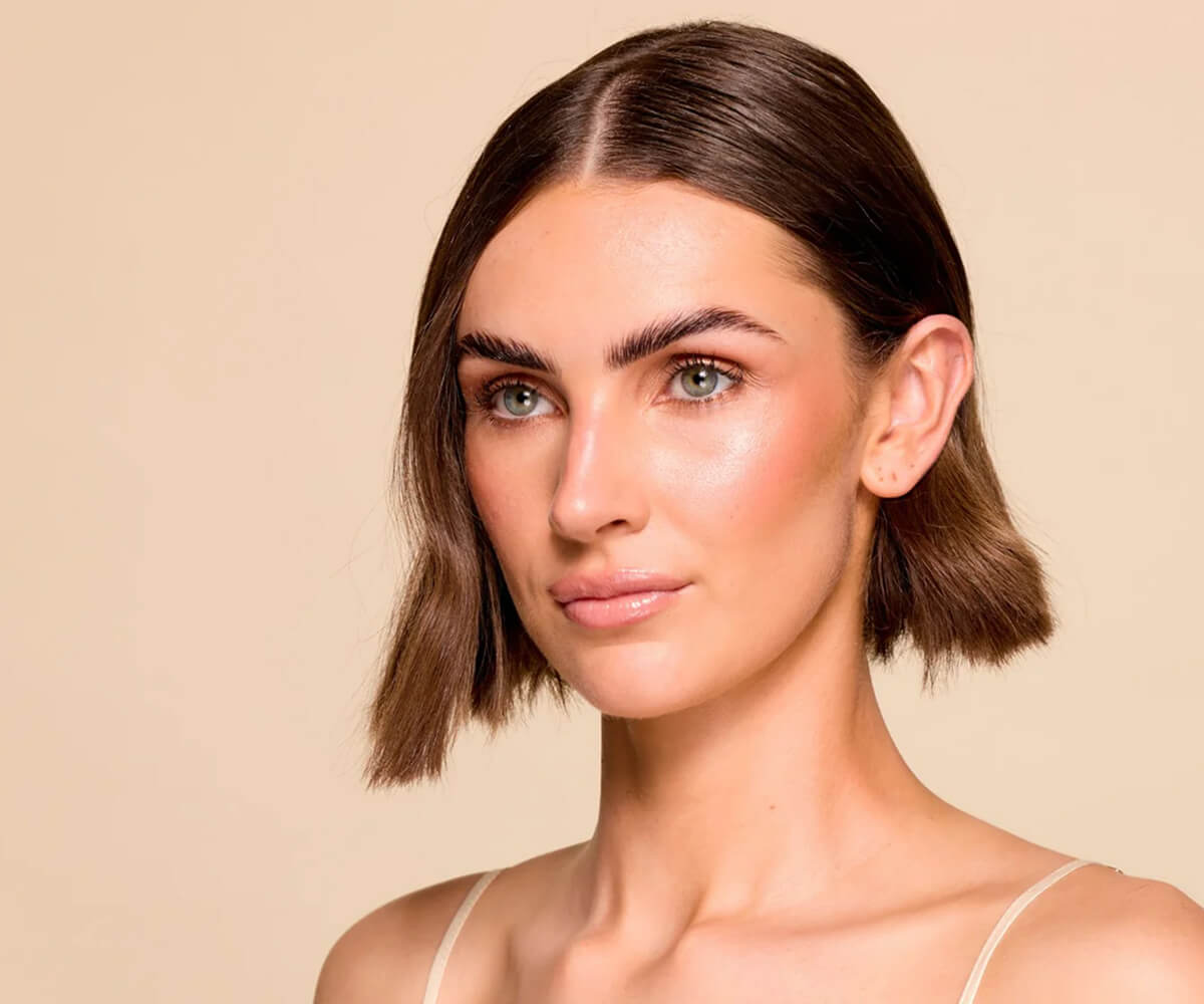 Young man and woman dressed in black and gray carrying matching gray bags with a textured pattern, standing in front of a circular-patterned wall.