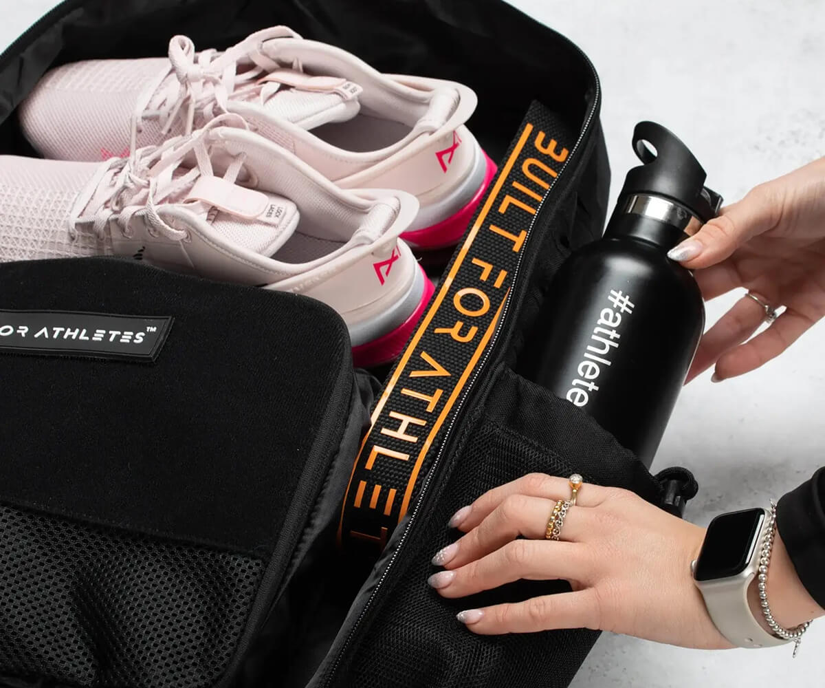 Young man and woman dressed in black and gray carrying matching gray bags with a textured pattern, standing in front of a circular-patterned wall.