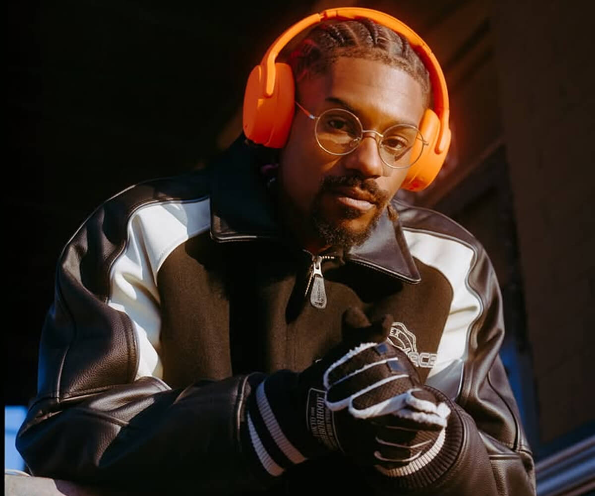 Young man and woman dressed in black and gray carrying matching gray bags with a textured pattern, standing in front of a circular-patterned wall.