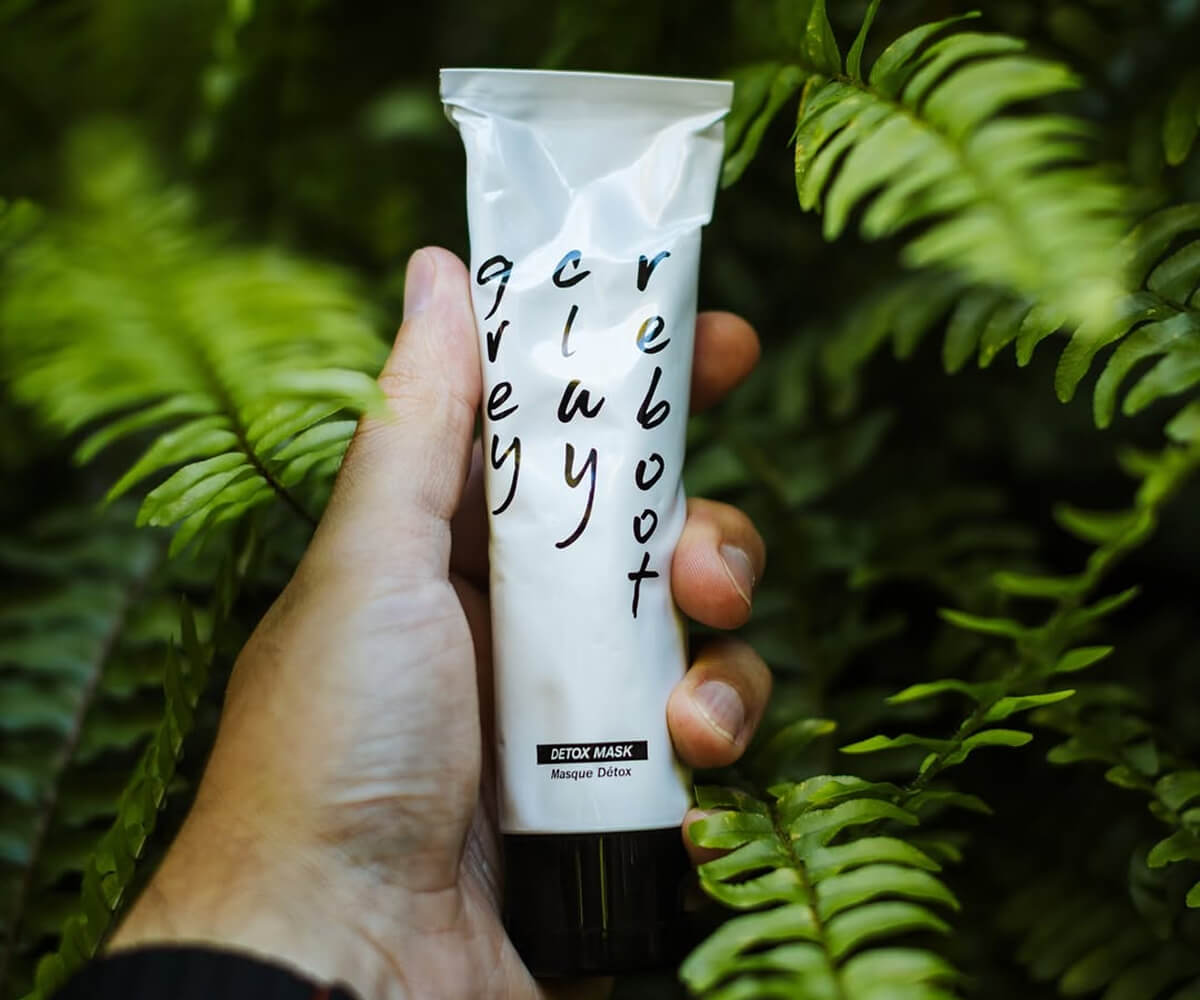 Young man and woman dressed in black and gray carrying matching gray bags with a textured pattern, standing in front of a circular-patterned wall.