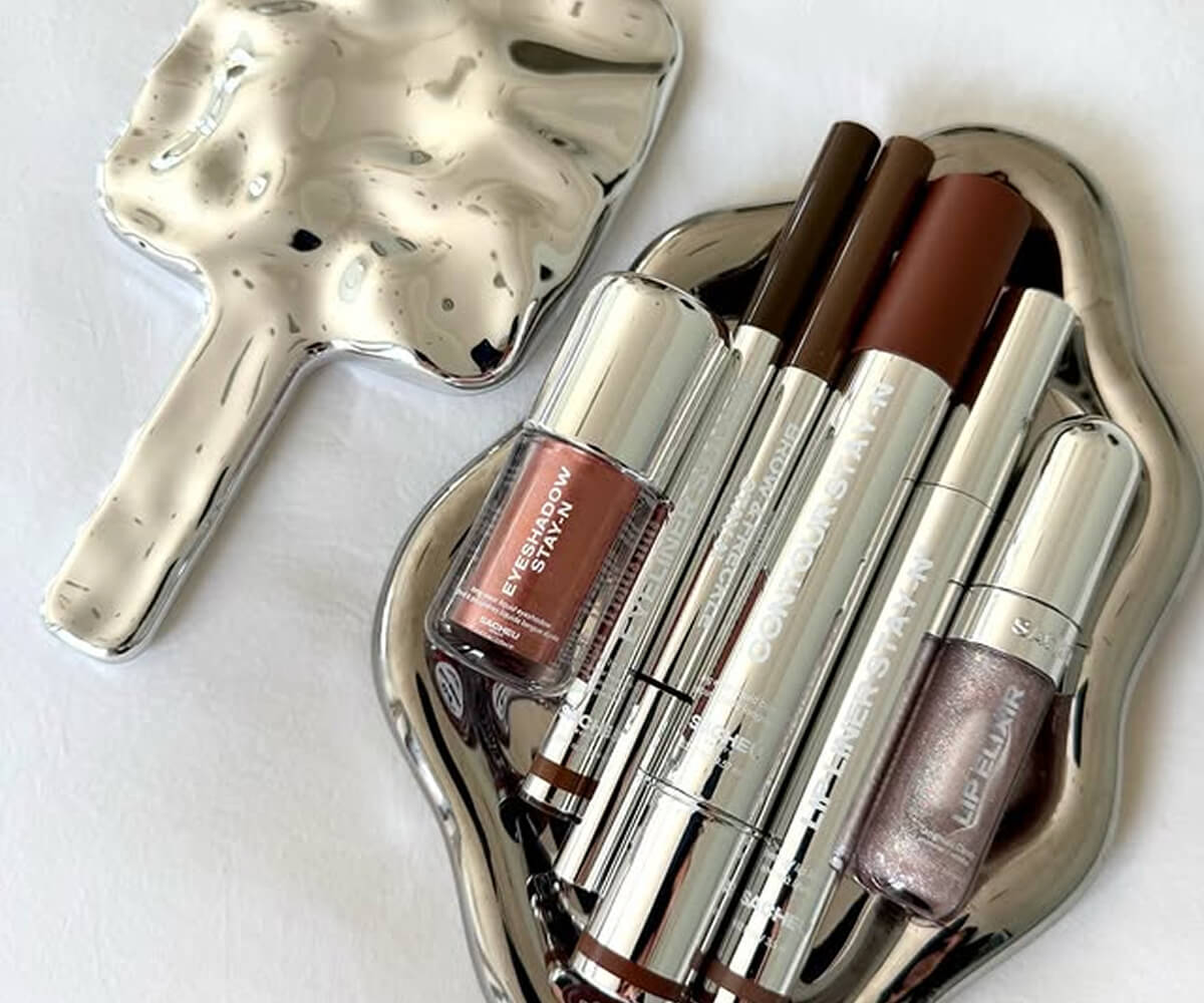 Young man and woman dressed in black and gray carrying matching gray bags with a textured pattern, standing in front of a circular-patterned wall.