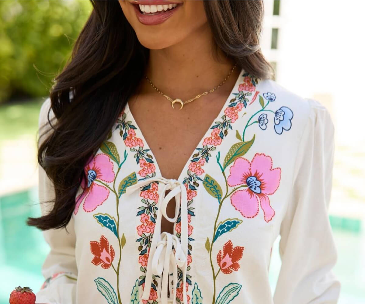 Close-up of a woman wearing a white blouse with colorful floral embroidery and a gold crescent moon necklace.