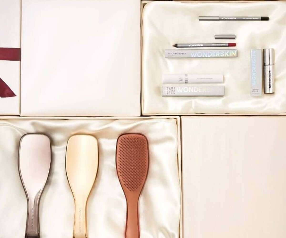 Three hairbrushes in different colors and a set of Wonderskin makeup products arranged on white satin fabric.