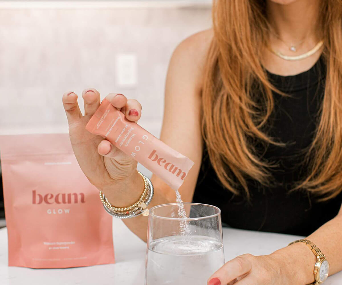 Woman pouring Beam Glow collagen supplement powder into a glass of water.