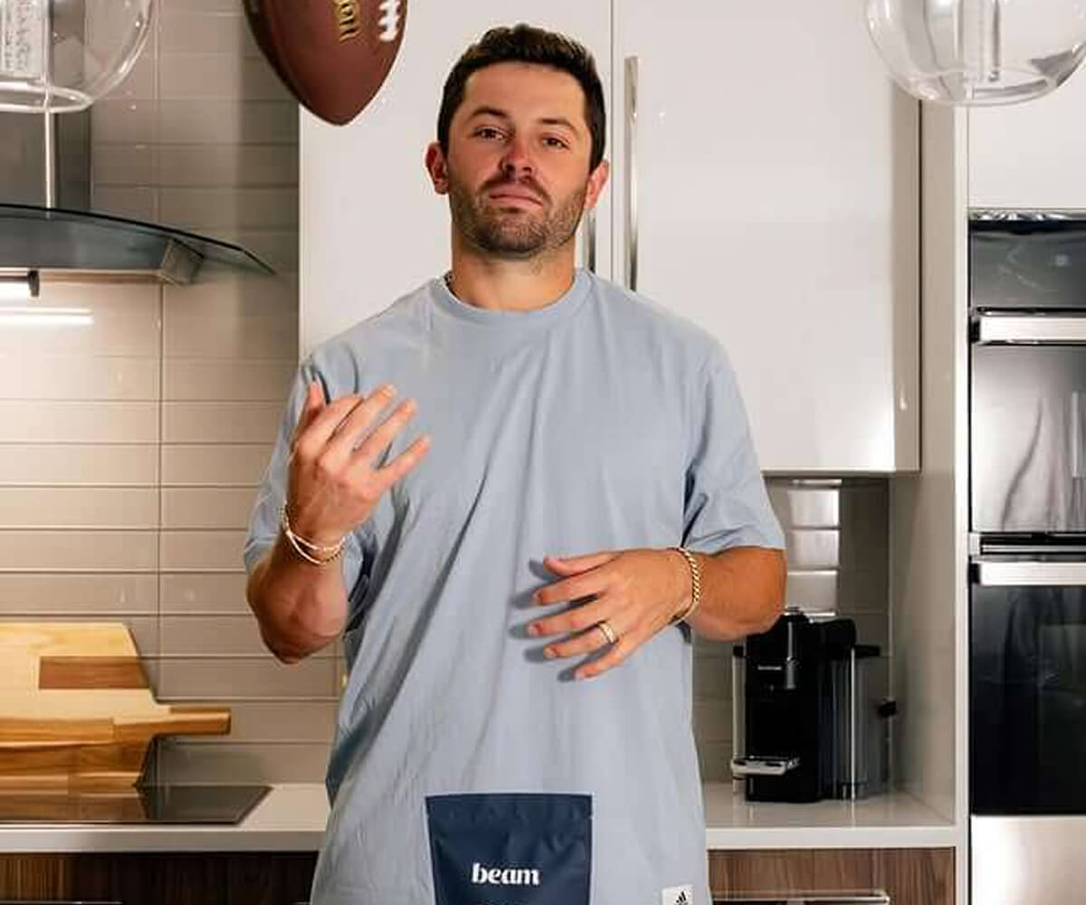 Man in a light blue 'beam' shirt standing in a modern kitchen gesturing with his hands.