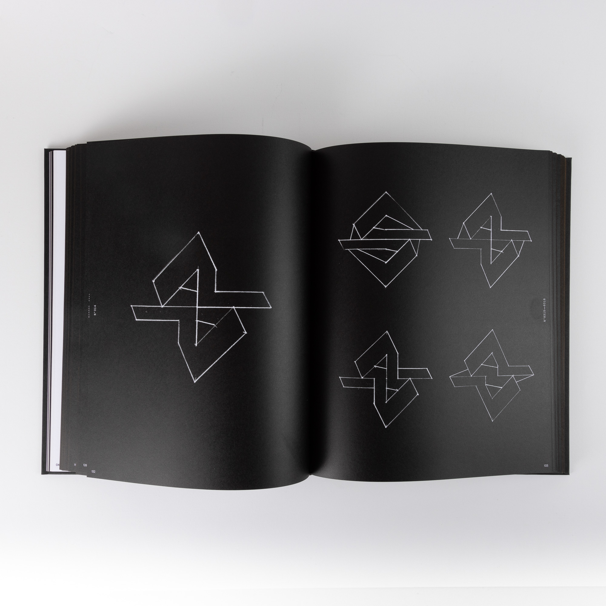 Open book with black pages showing multiple white geometric line designs resembling abstract shapes.