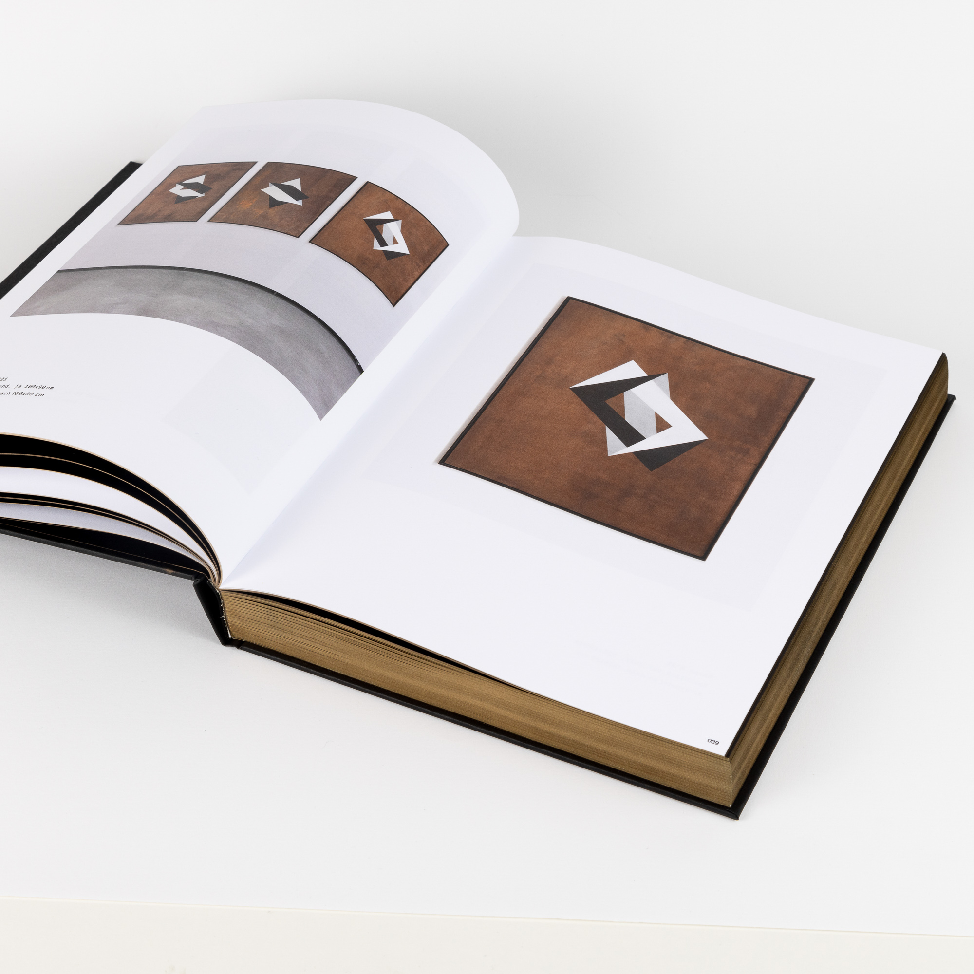 Open art book displaying geometric abstract artwork with overlapping angular shapes in black, white, and brown tones.