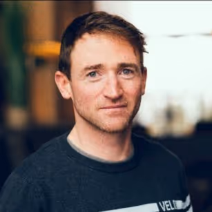Man with short brown hair wearing a dark gray sweater, posing indoors with a blurred background.