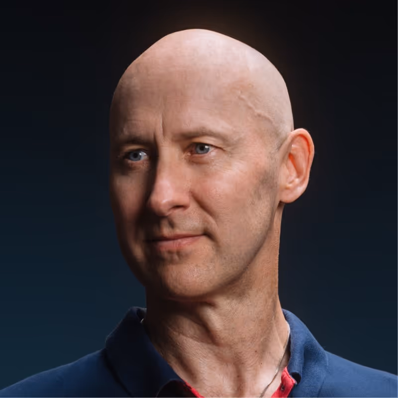 Portrait of a bald man with blue eyes wearing a dark blue collared shirt against a dark background.