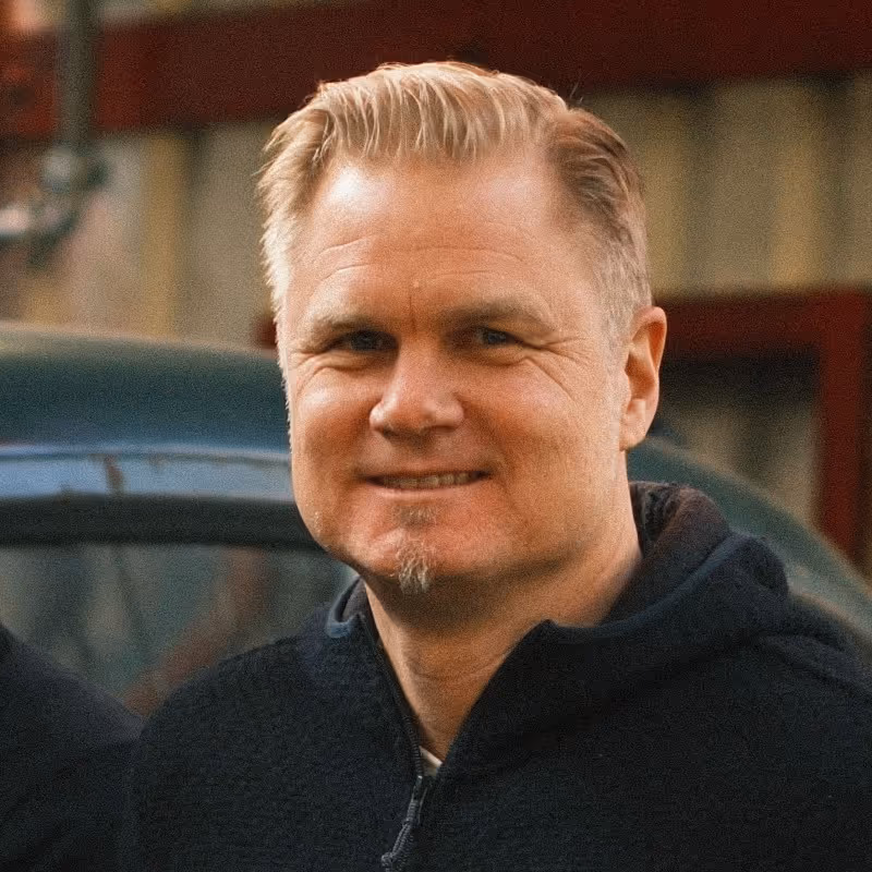 Smiling middle-aged man with blond hair and a short goatee wearing a dark zip-up jacket outdoors.