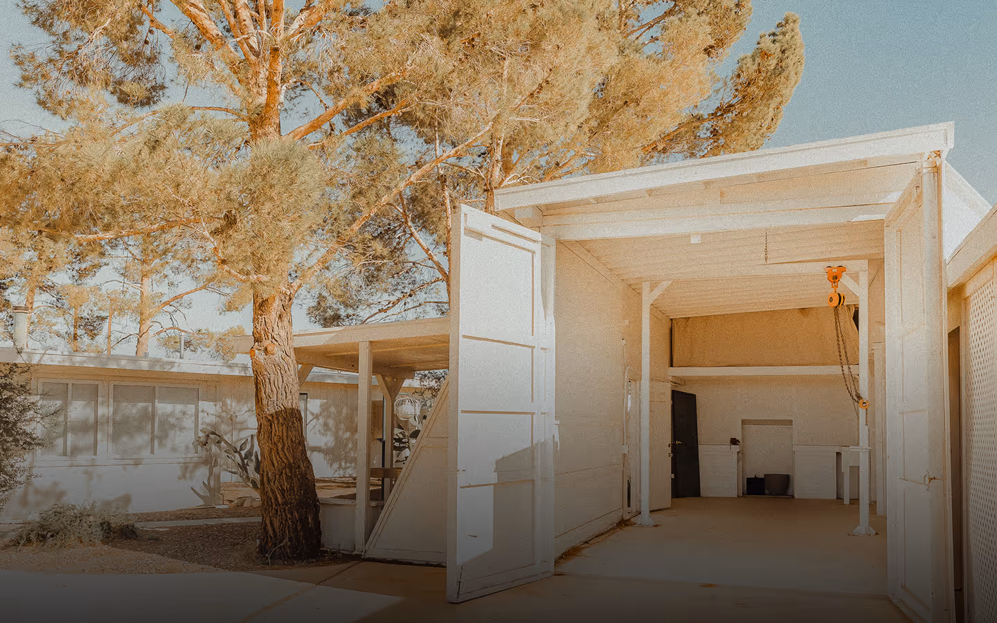 Open, spacious white garage with a pulley hoist system and large pine trees in the background.