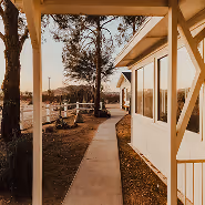 Pathway beside a white building with large windows and trees lining the sidewalk at sunset.