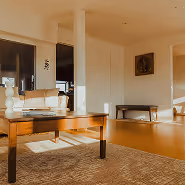 Sunlit living room with a wooden coffee table, cushioned bench, and framed artwork on the wall.