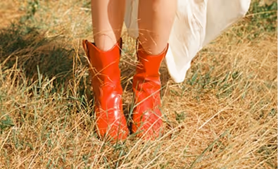 Person wearing shiny red boots standing on dry grass with a flowing white garment.