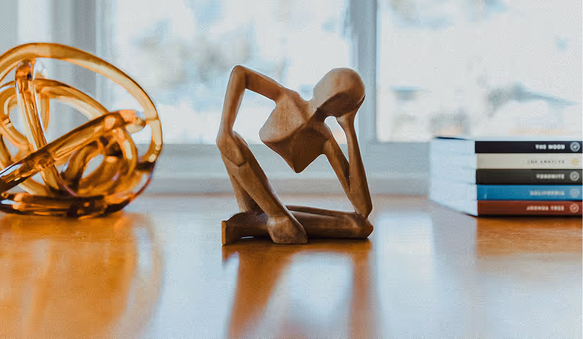 A wooden sculpture of a man bending over next to a book.