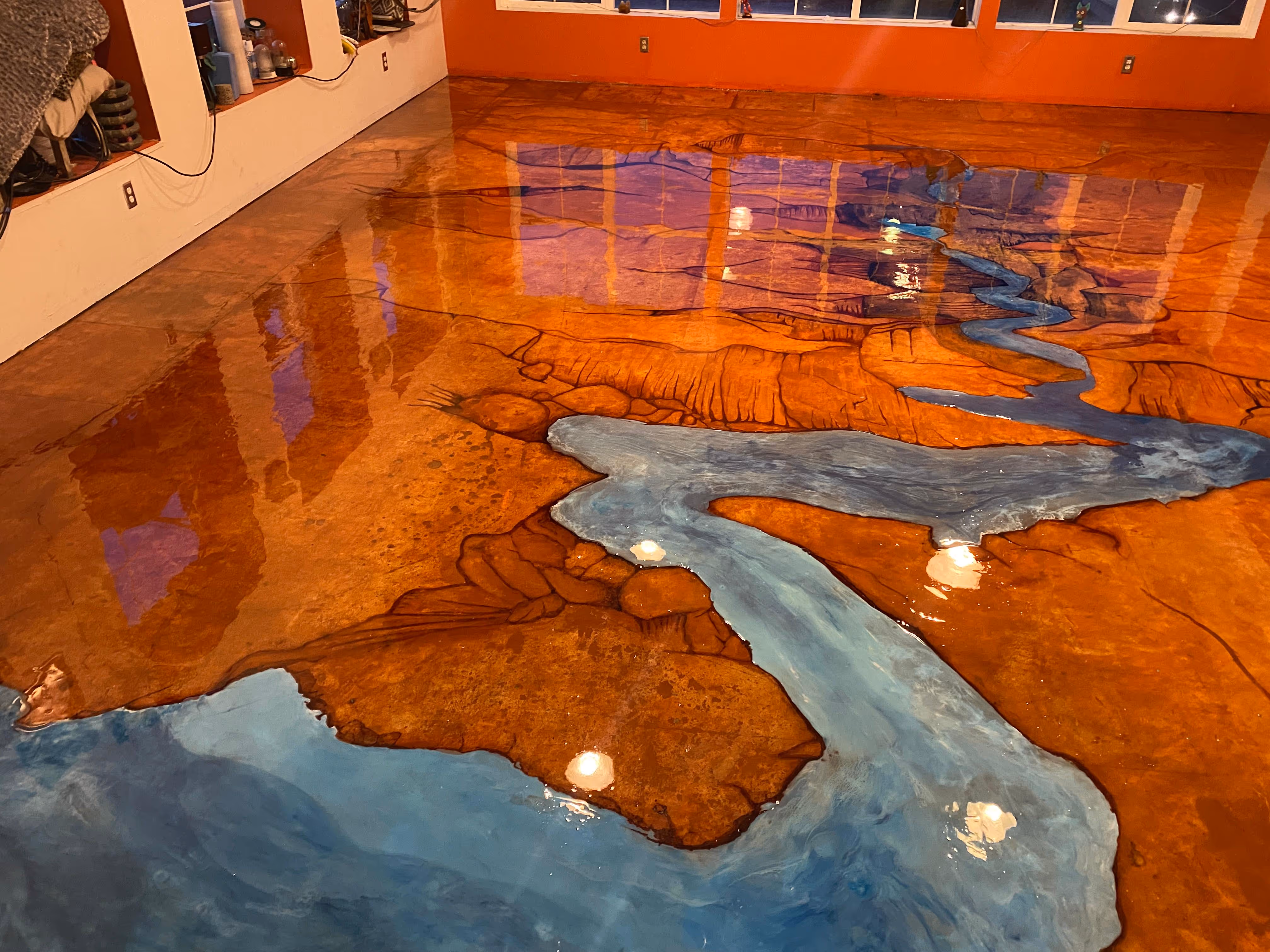 Glossy polished floor painted with a blue river flowing through brown land with rock-like textures indoors.