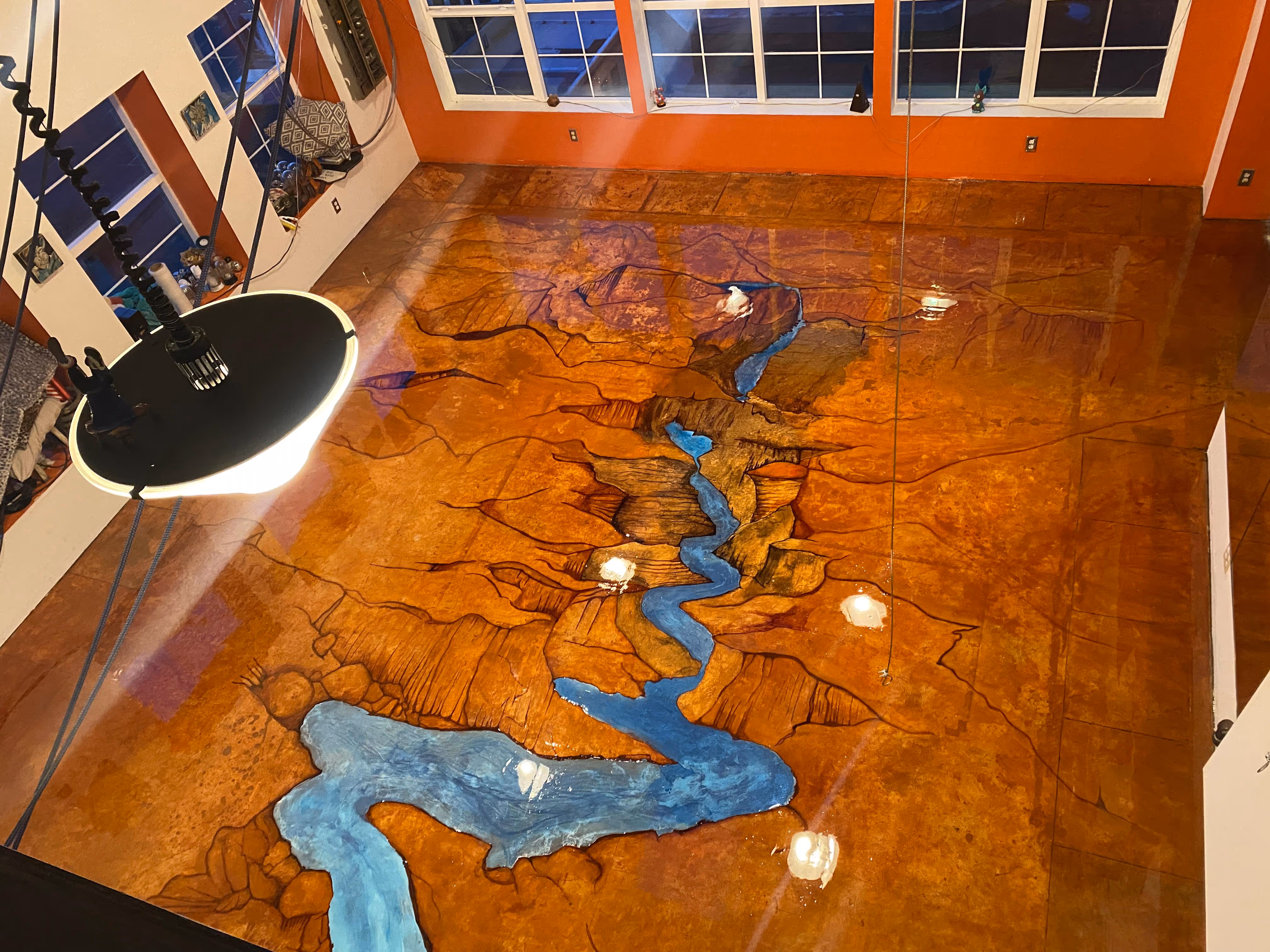 Glossy floor with a painted canyon and river design inside a room with orange walls and large windows.