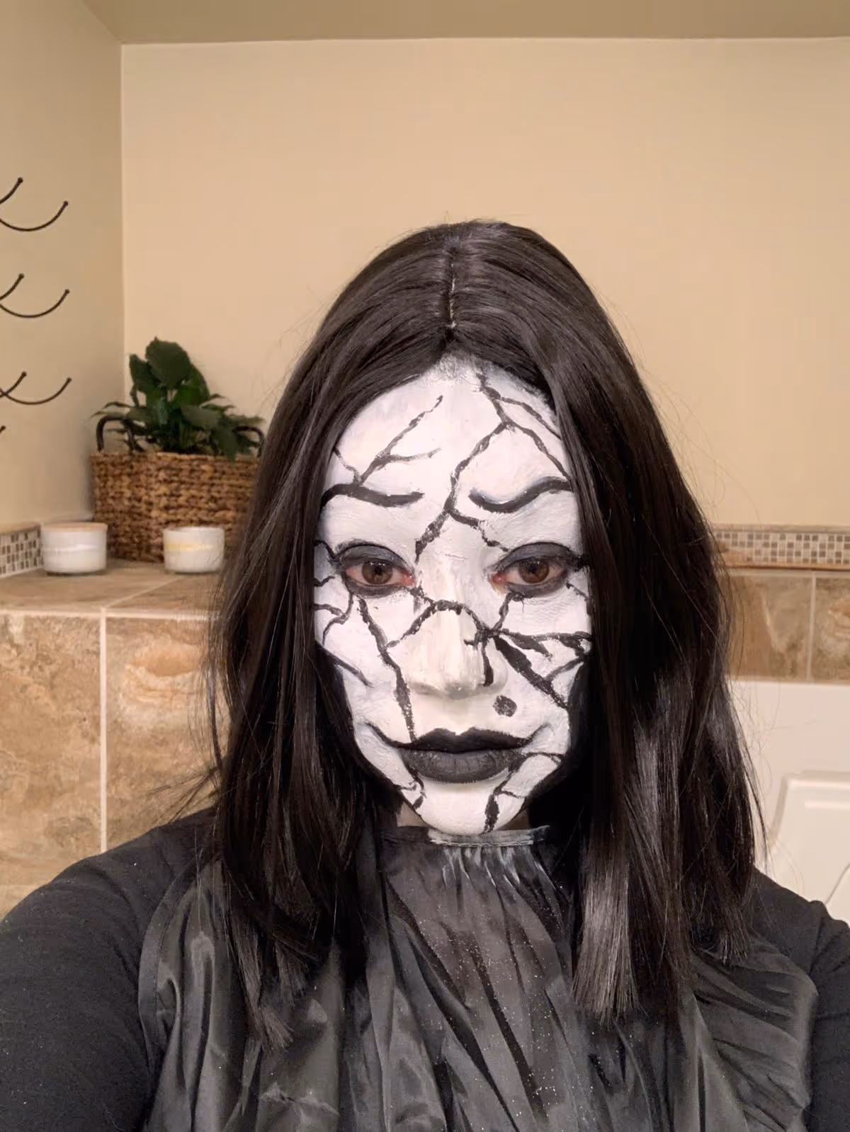 Person with black wig and face painted white with black crack-like lines resembling broken porcelain.