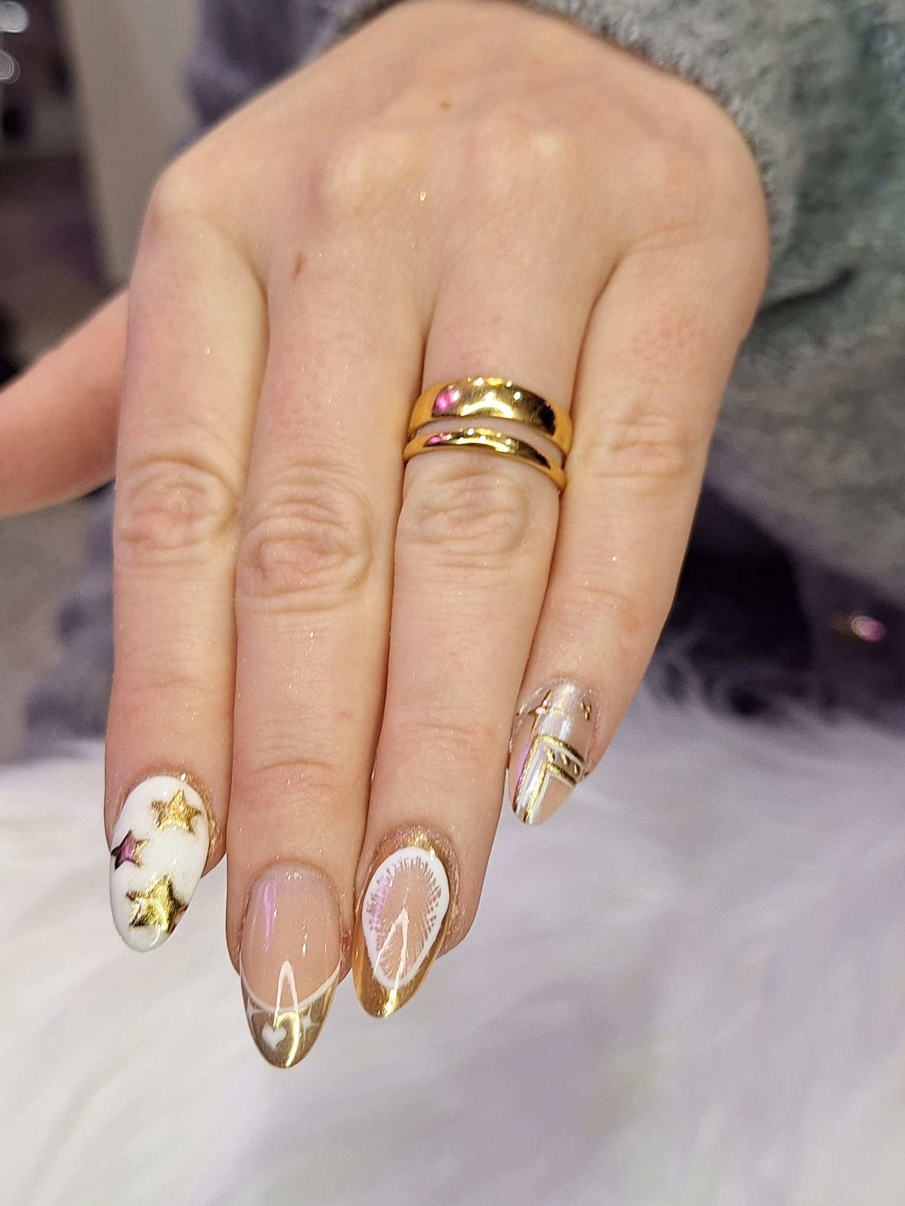 Eine Hand mit weiß-goldenem Nageldesign mit goldenen Sternen – festliche Maniküre