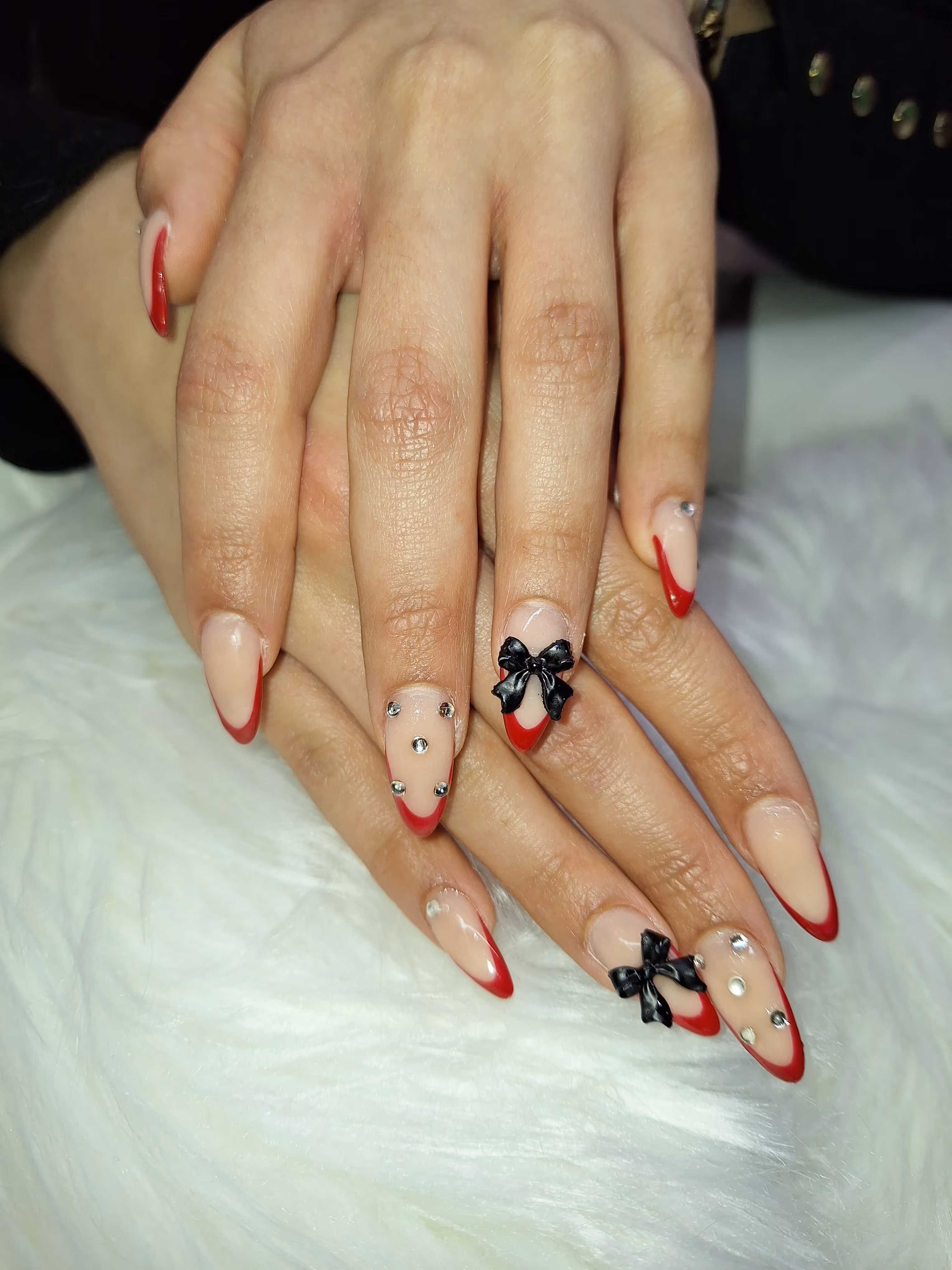 Hands with nude and red French tip manicure decorated with black bows and silver rhinestones.