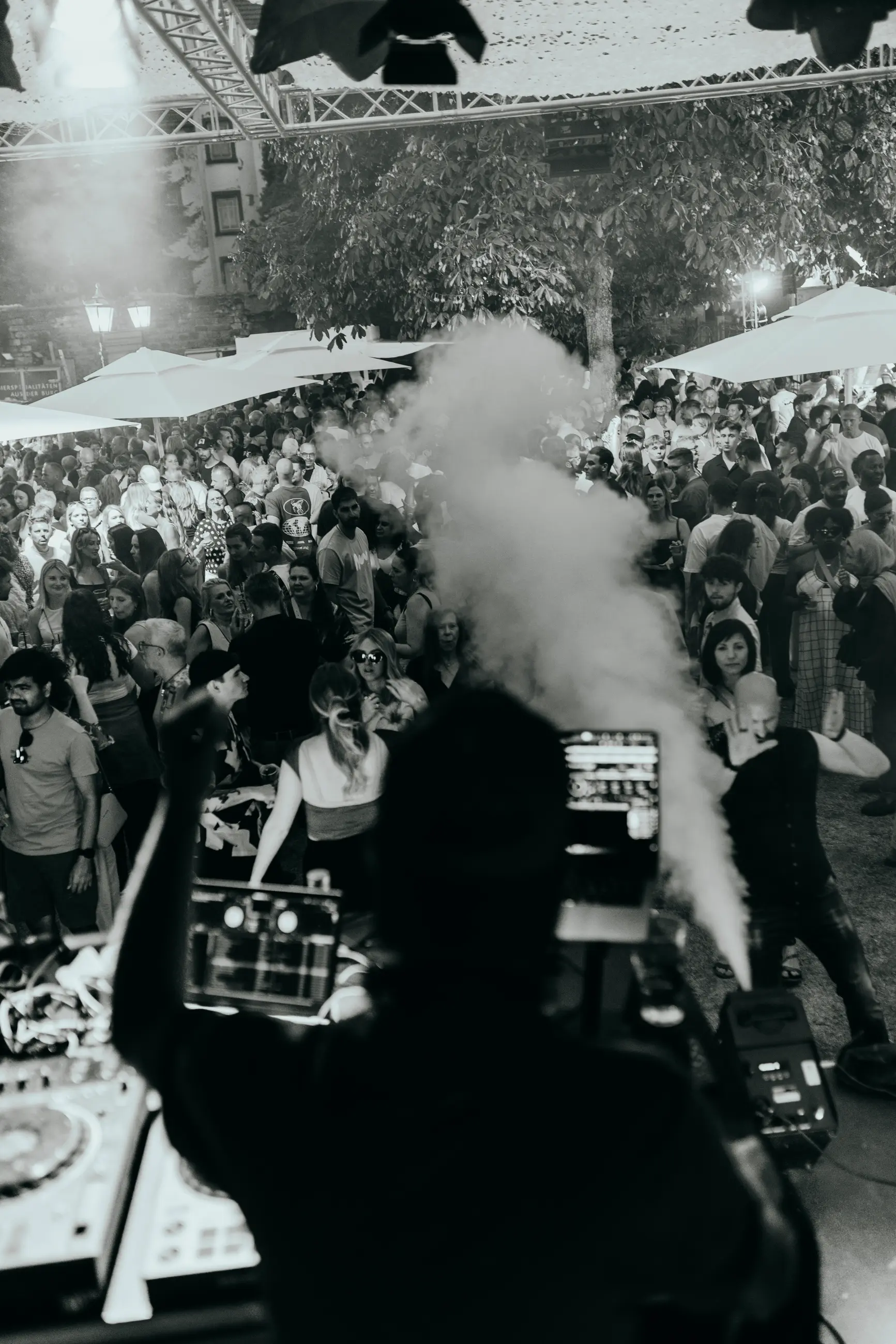 DJ steht hinter einem Mischpult und legt bei einer großen Menschenmenge auf einer Outdoor-Party auf.