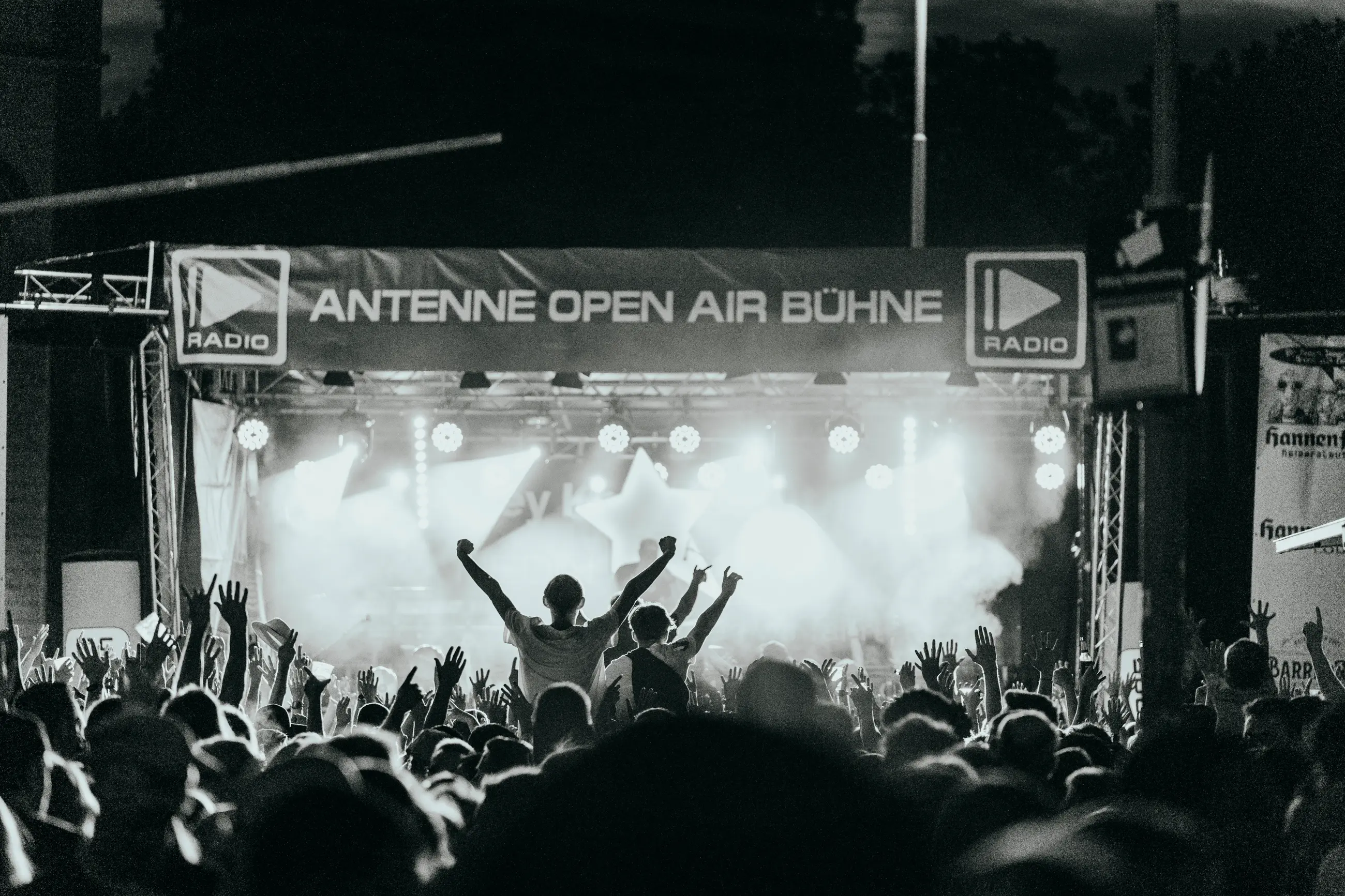 Große Menschenmenge mit erhobenen Armen bei einem nächtlichen Open-Air-Konzert vor einer beleuchteten Bühne.