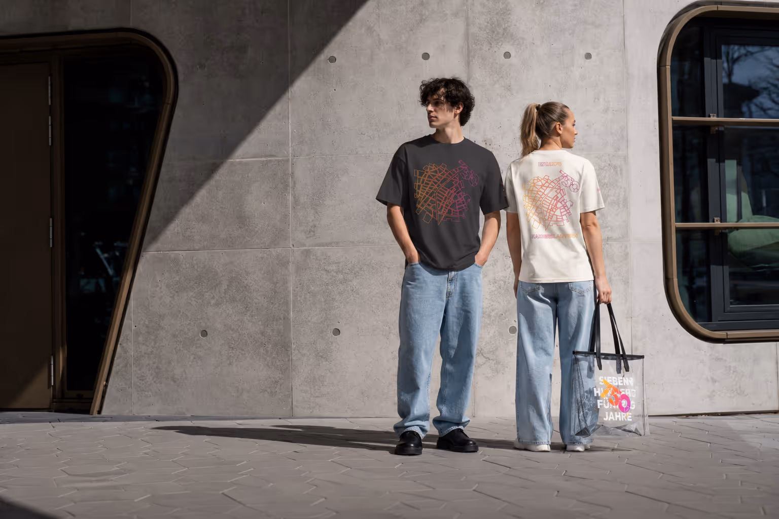 Junge und Frau tragen T-Shirts mit buntem abstraktem Muster vor grauer Betonwand.