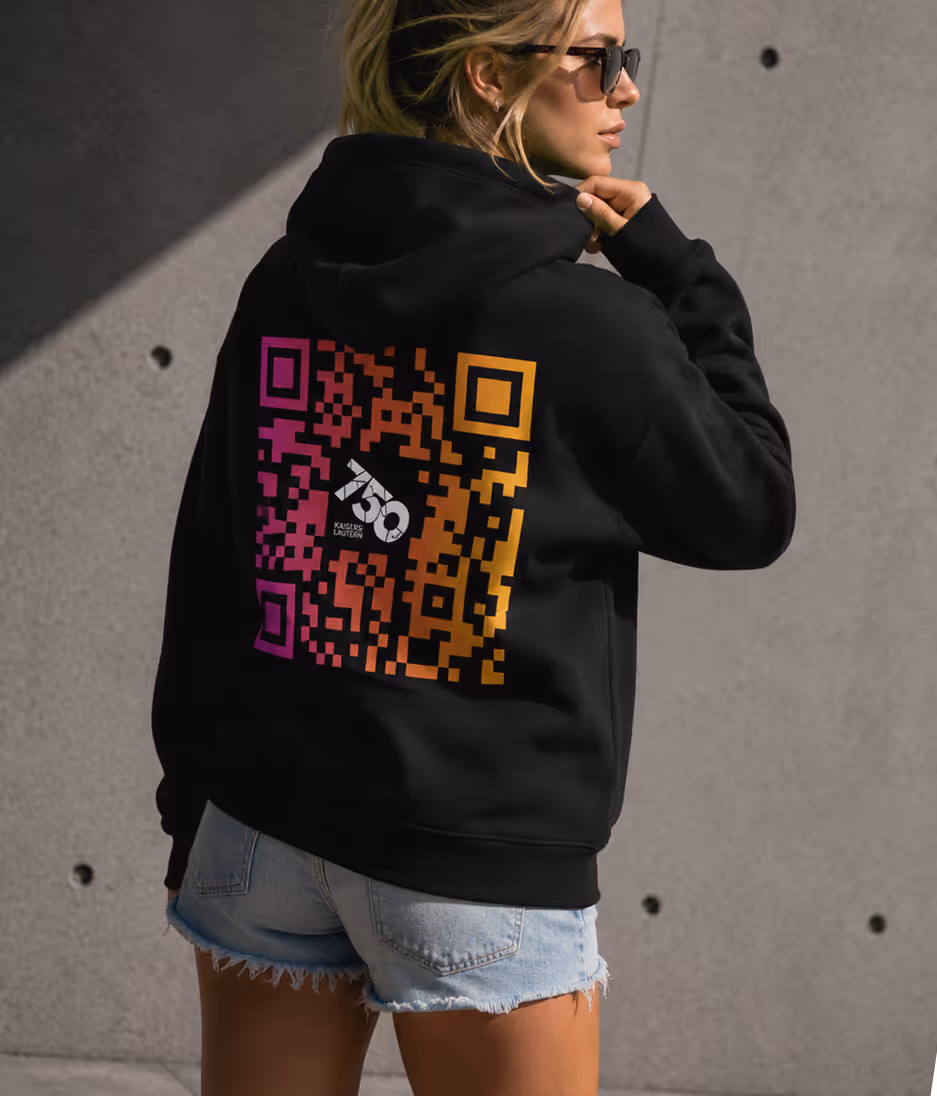 Frau trägt schwarzen Kapuzenpullover mit farbigem QR-Code auf dem Rücken und hellen Jeansshorts.