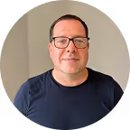 Muškarac s naočalama i tamnom majicom stoji ispred bijele pozadine.