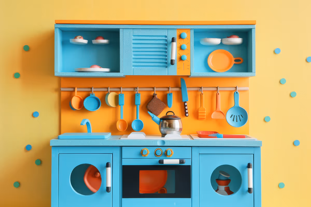 Šarena igračka kuhinja plavo-narandžaste boje sa posudama, priborom i plavim zidom u pozadini.