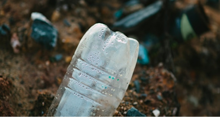 Better Flags | CiClO Flags | Close-up of a discarded plastic bottle lying on the ground among dirt and debris.