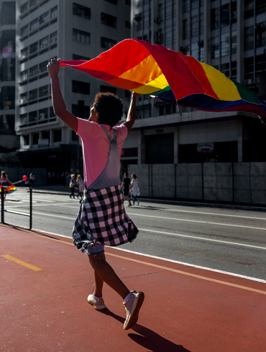 Better Flags | CiClO Flags | Person walking on a city street holding a large rainbow pride flag above their head.