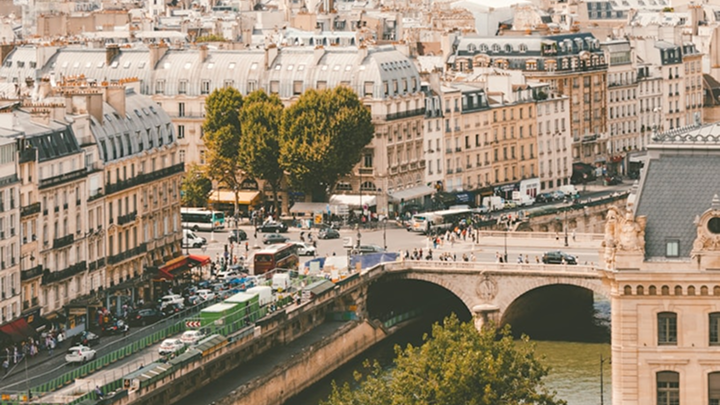 Better Flags | CiClO Flags | Urban view of a Parisian street with classic buildings, a bridge over the river Seine, and trees lining the area.