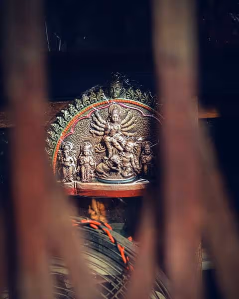 Sculpture hindoue détaillée représentant une déesse à plusieurs bras entourée d'autres figures divines, vue à travers un cadre flou.