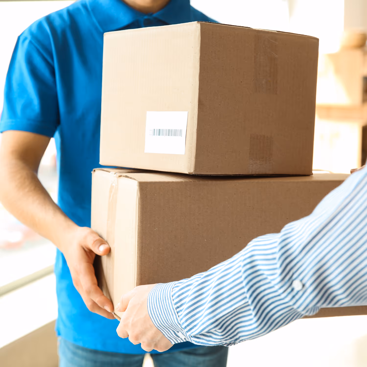 Person in blue shirt handing over two stacked cardboard boxes to another person wearing a blue and white striped shirt.