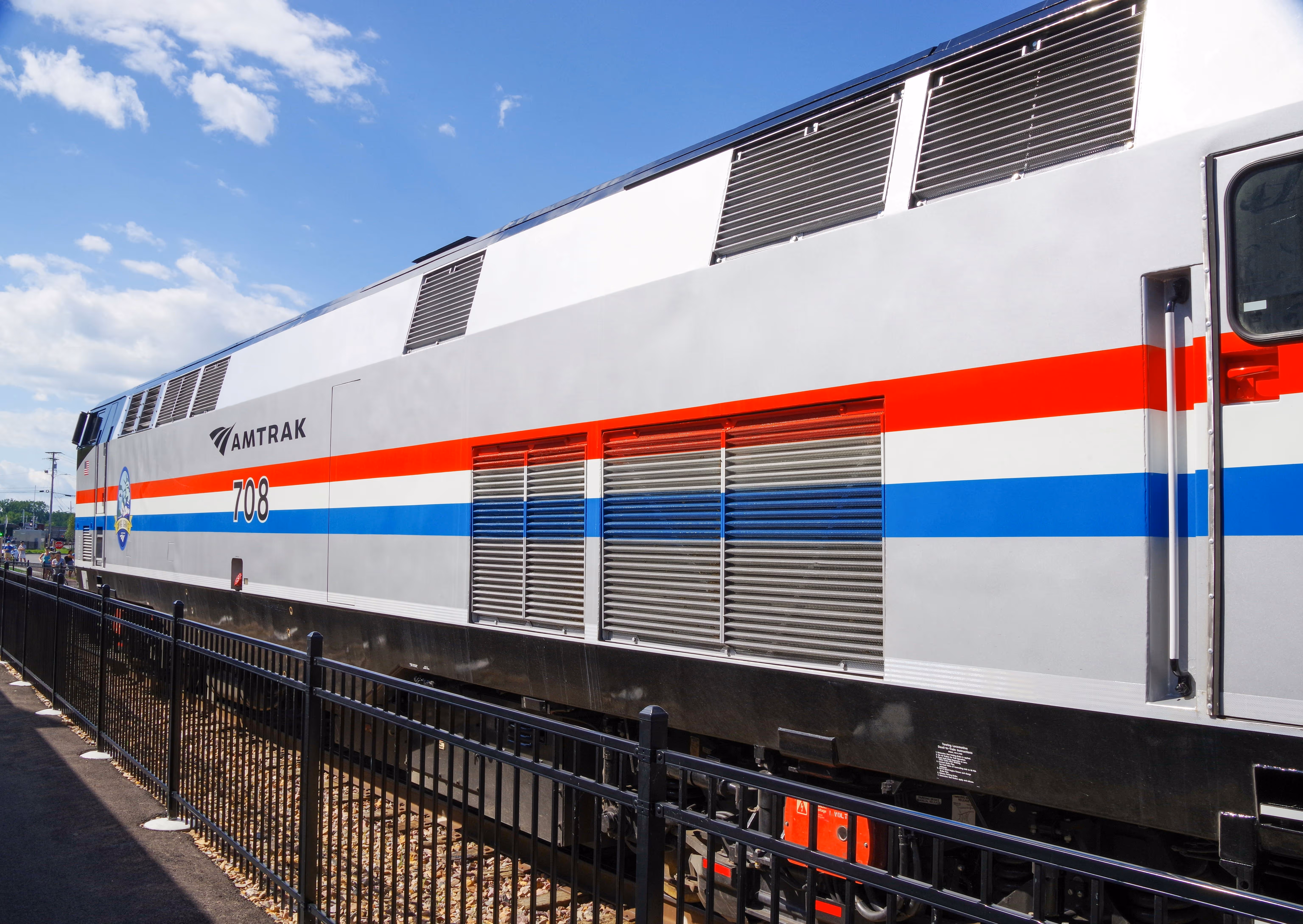 Side view of an Amtrak passenger train engine with red and blue stripes under a partly cloudy sky.