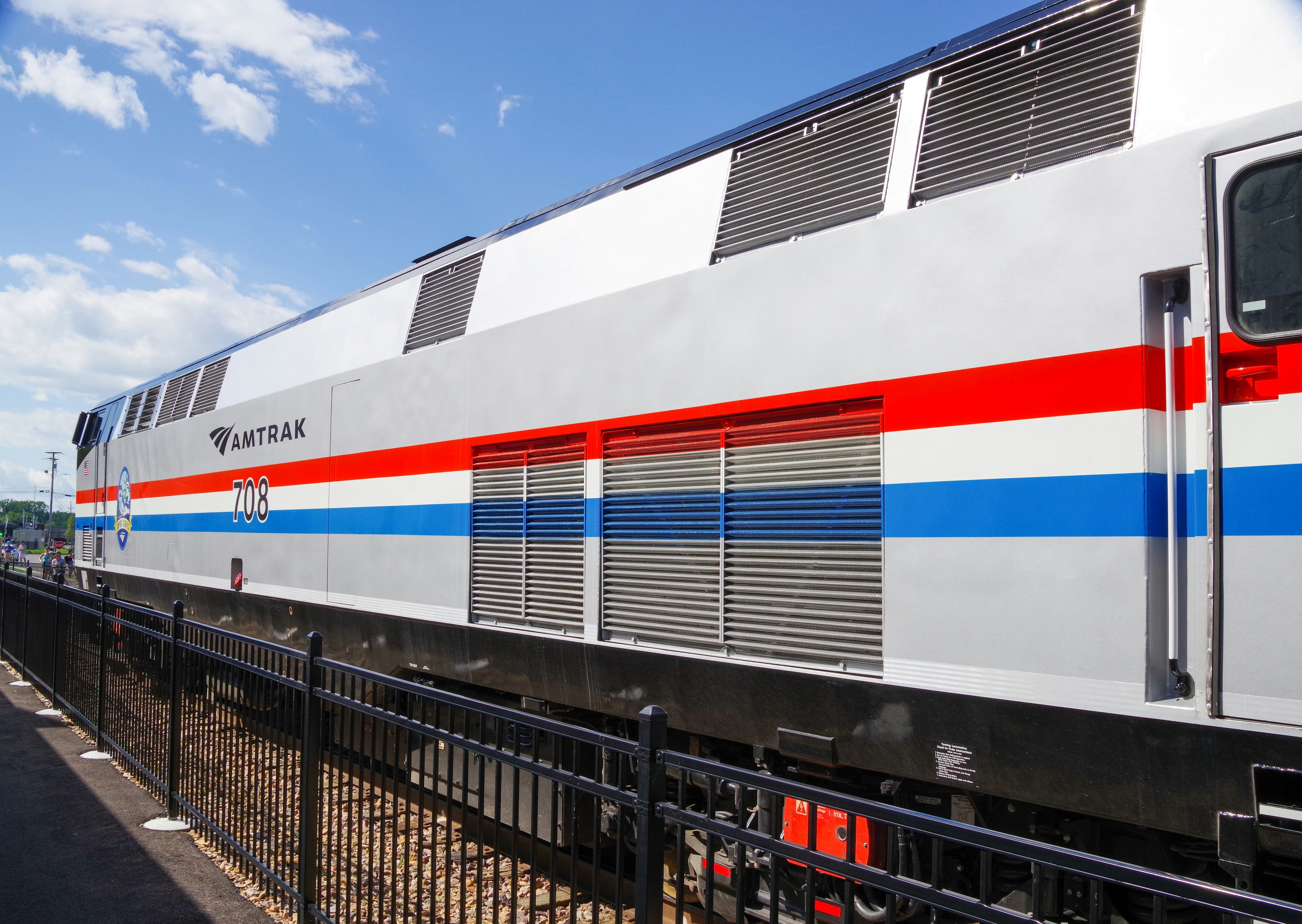 Side view of an Amtrak passenger train engine with red and blue stripes under a partly cloudy sky.