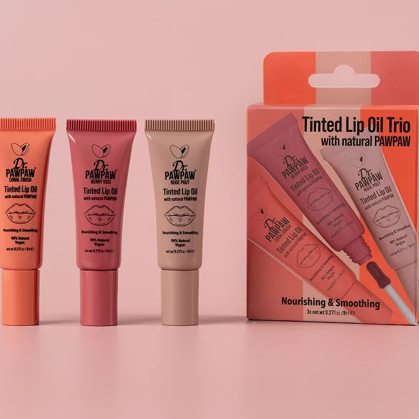 Three tubes of Dr. Pawpaw tinted lip oil in coral, berry, and nude shades next to their packaging labeled Tinted Lip Oil Trio with natural PAWPAW.