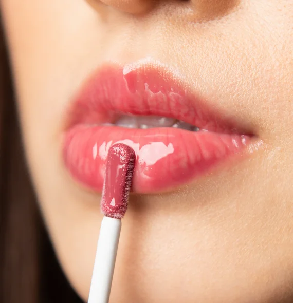 Close-up of a person applying glossy pink lip gloss to their lips with an applicator wand.