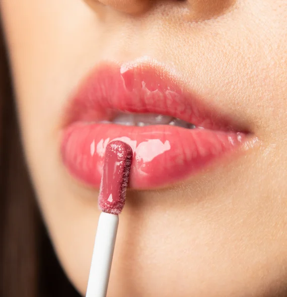 Close-up of lips applying glossy pink lip gloss with a white applicator wand.
