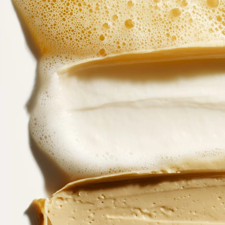 Close-up of whipped coffee foam layered over creamy coffee mixture on a light background.