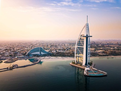 Aerial view of the Burj Al Arab hotel on its man-made island near Dubai coastline at sunset.