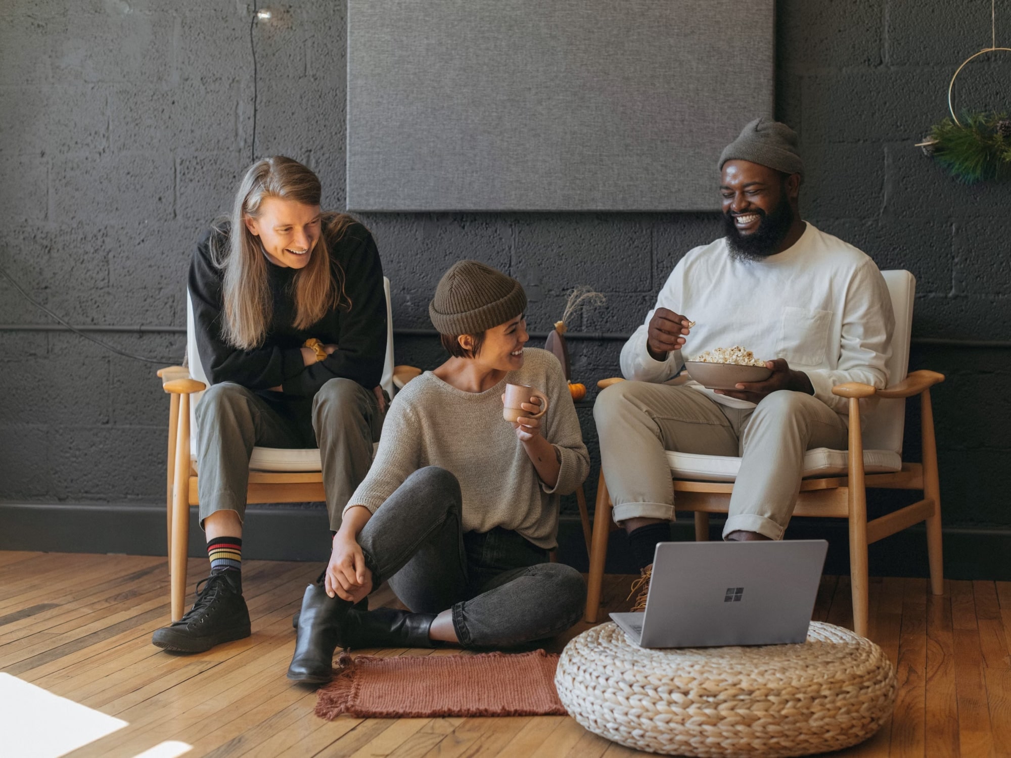 Three friends enjoying snacks and drinks while watching a laptop in a cozy room.