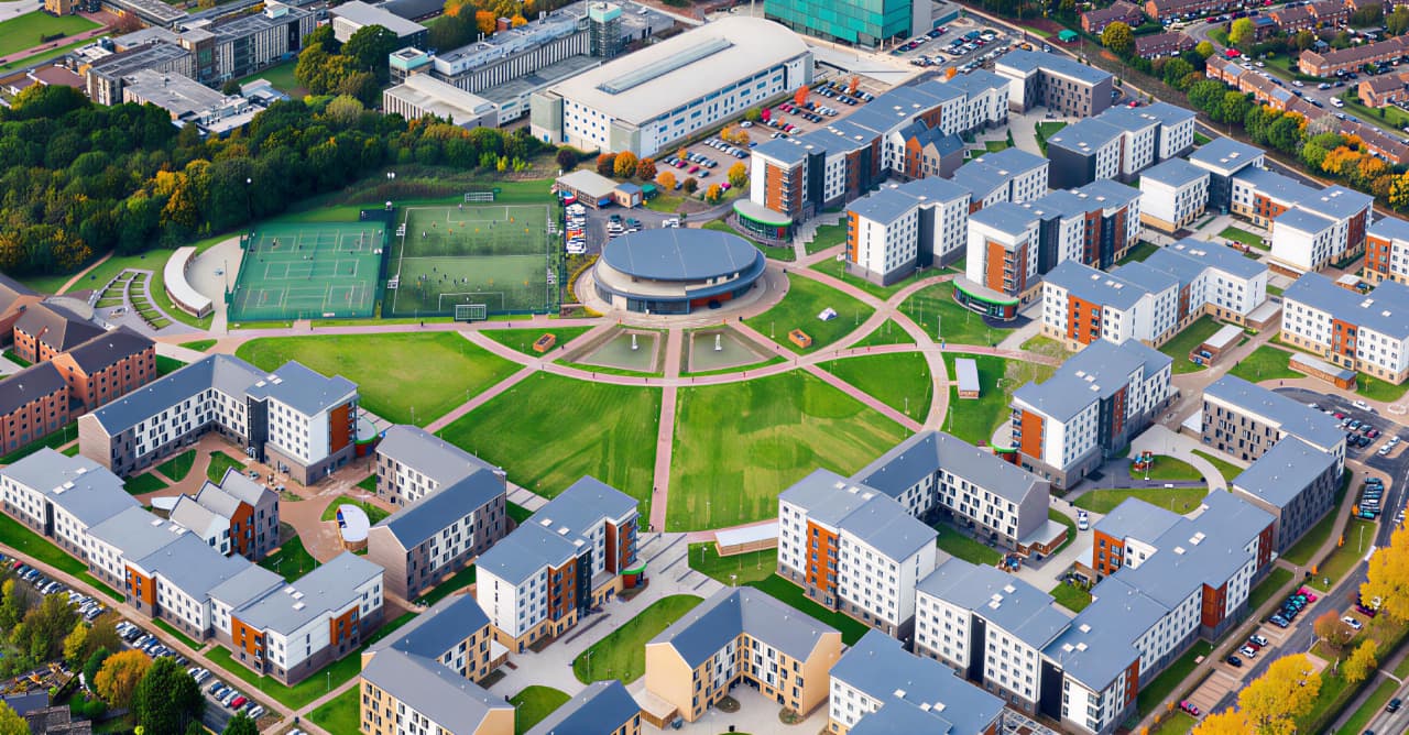 Aerial view of a large modern campus with multiple residential buildings arranged in geometric patterns around a central circular lawn and sports fields.