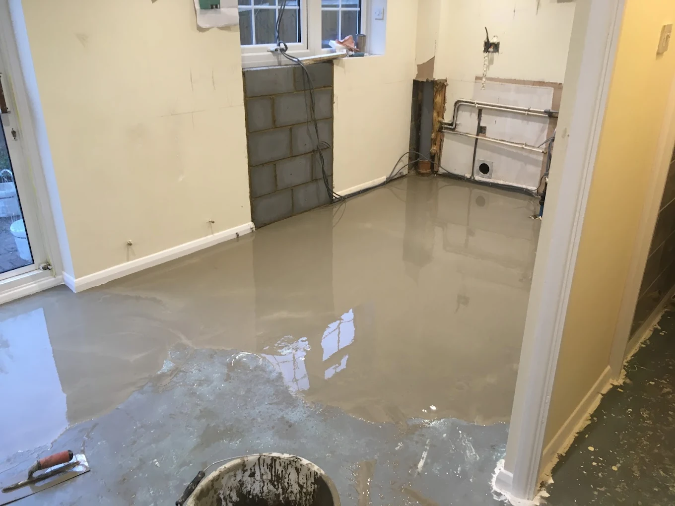 Room under renovation with freshly poured smooth cement floor drying near walls and window.